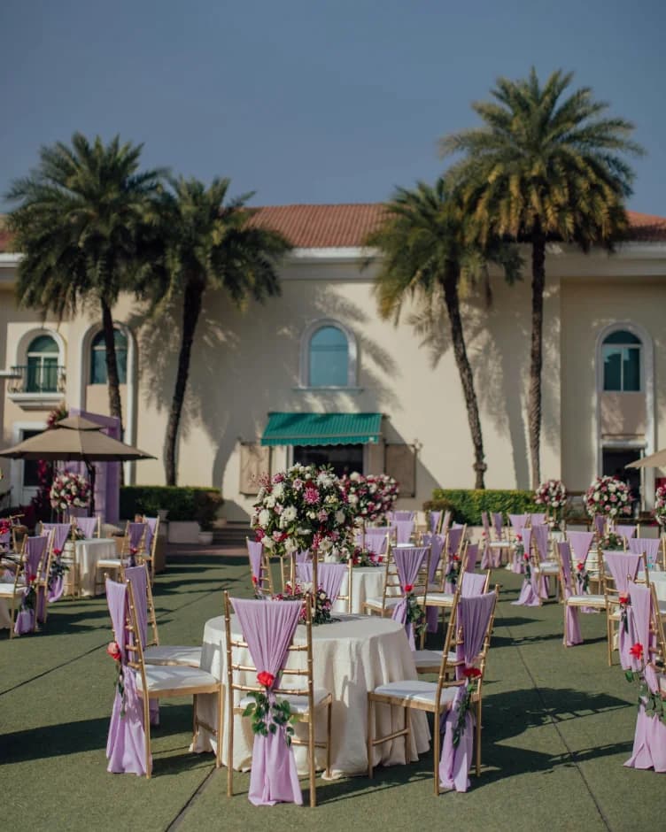 Round tables with lilac chair sashes and rose centerpieces on a lawn lined with palm trees