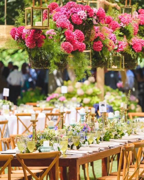 Hanging baskets of pink hydrangeas above long wooden tables at an outdoor reception