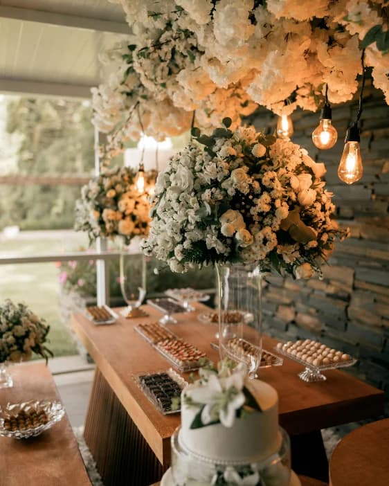 A dessert table beneath a cloud of white flowers and glowing bulbs