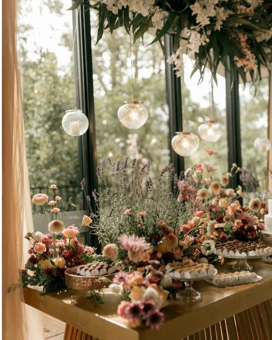A dessert table of lavender, roses and dahlias under hanging glass lanterns