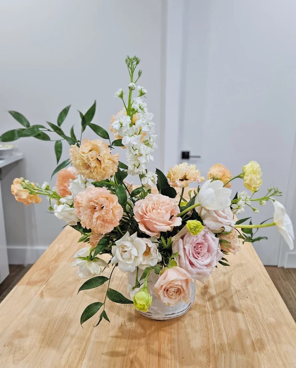 A peach and white arrangement in a ceramic vase on a wooden dining table