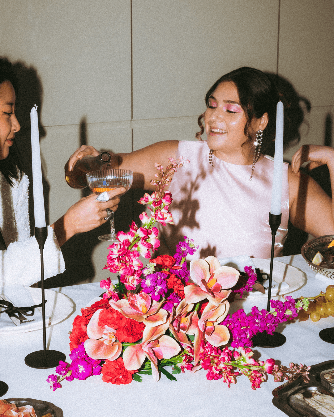 Guests toasting over a low centerpiece of orchids, carnations and magenta stock between tall candles