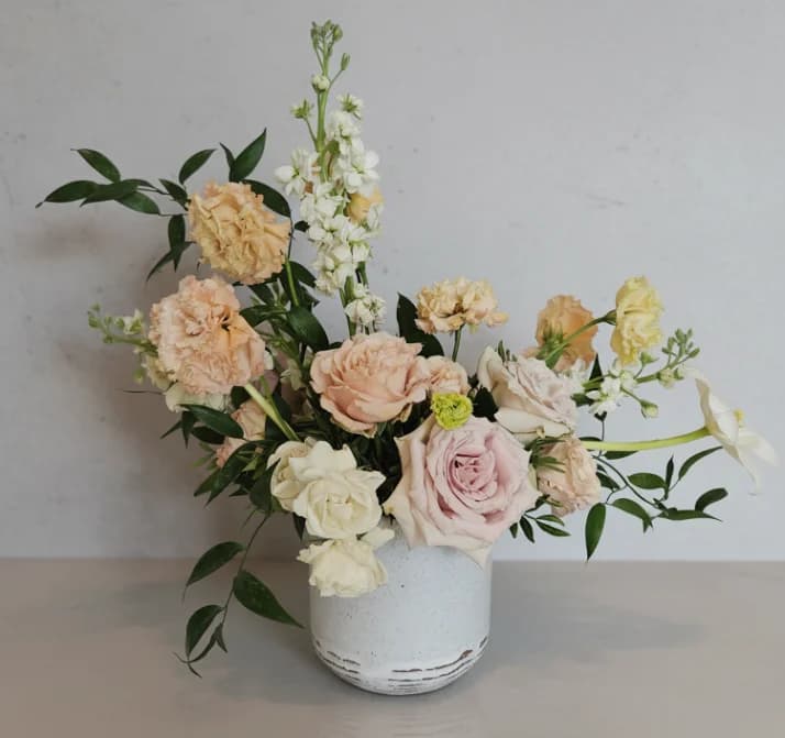 A soft peach and blush arrangement of roses, carnations and stock in a speckled ceramic pot