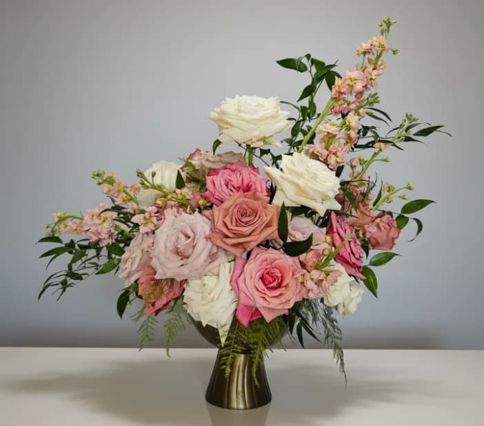 Pink, coral and white roses with stock in a brass vase