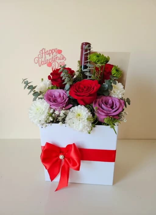 A Valentine’s Day gift box of red and purple roses with white chrysanthemums, a bottle of wine and a red bow