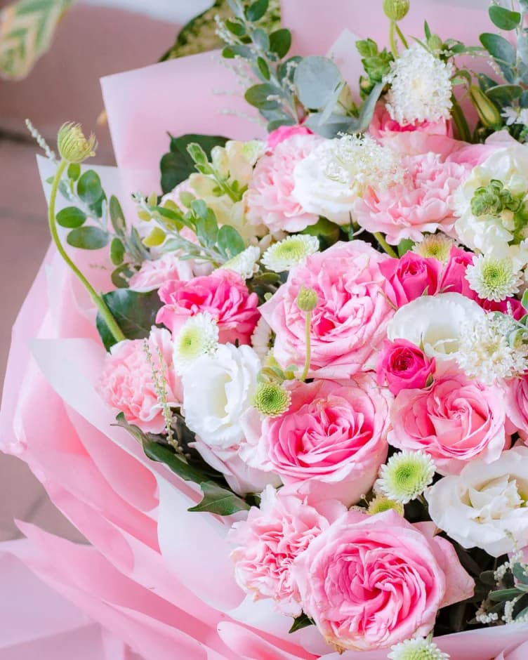 A bouquet of pink roses, carnations and white lisianthus wrapped in pink paper
