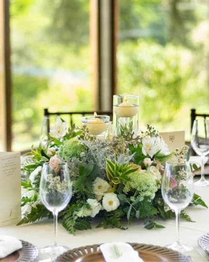 A low white and green centerpiece with floating candles on a reception table